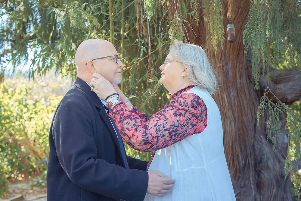 A couple shares a tender moment together outdoors among tall redwood trees in a scenic forest setting.
