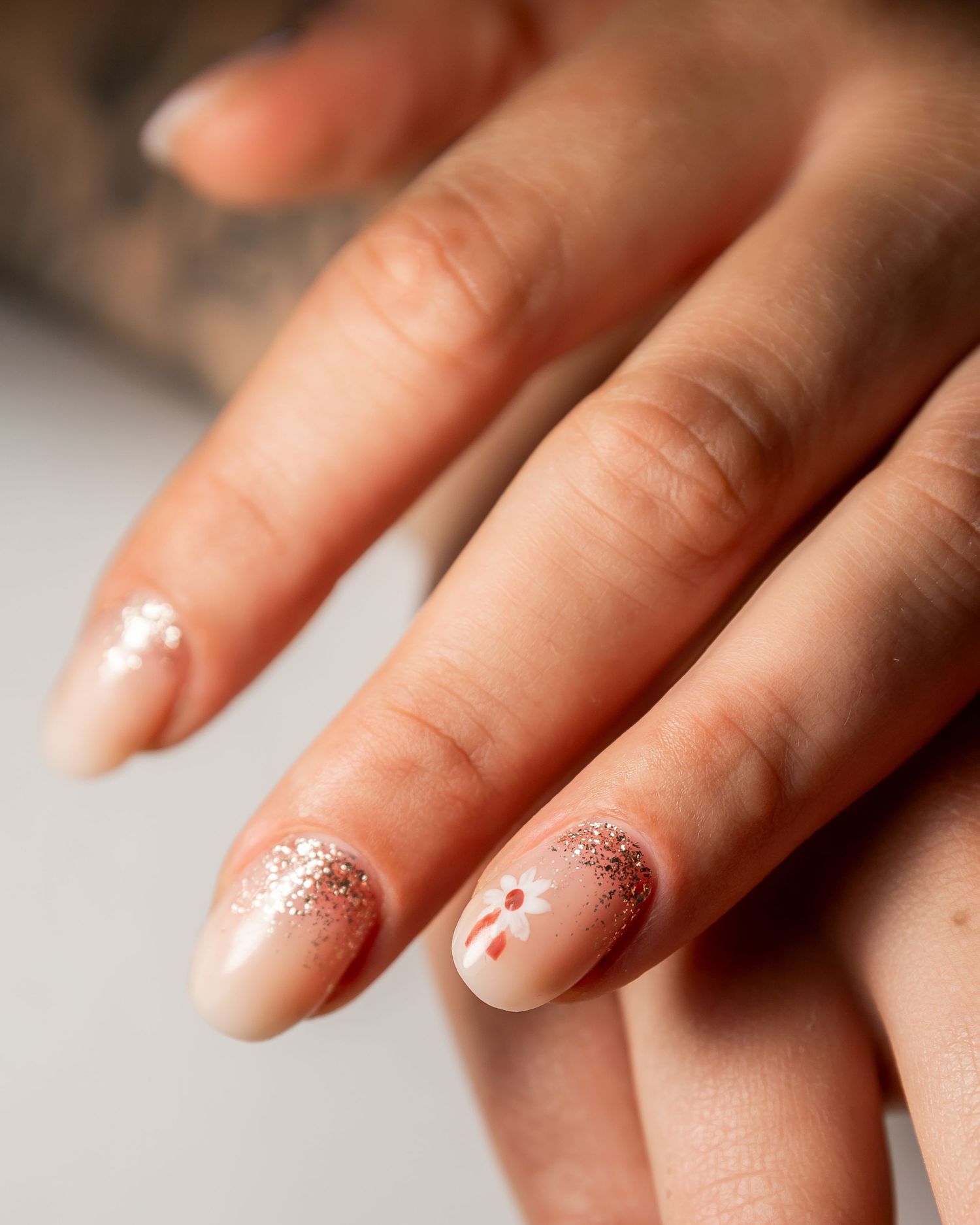 Close-up of a manicured hand showing glittery pink ombre nail art with delicate minimalist accent dots.
