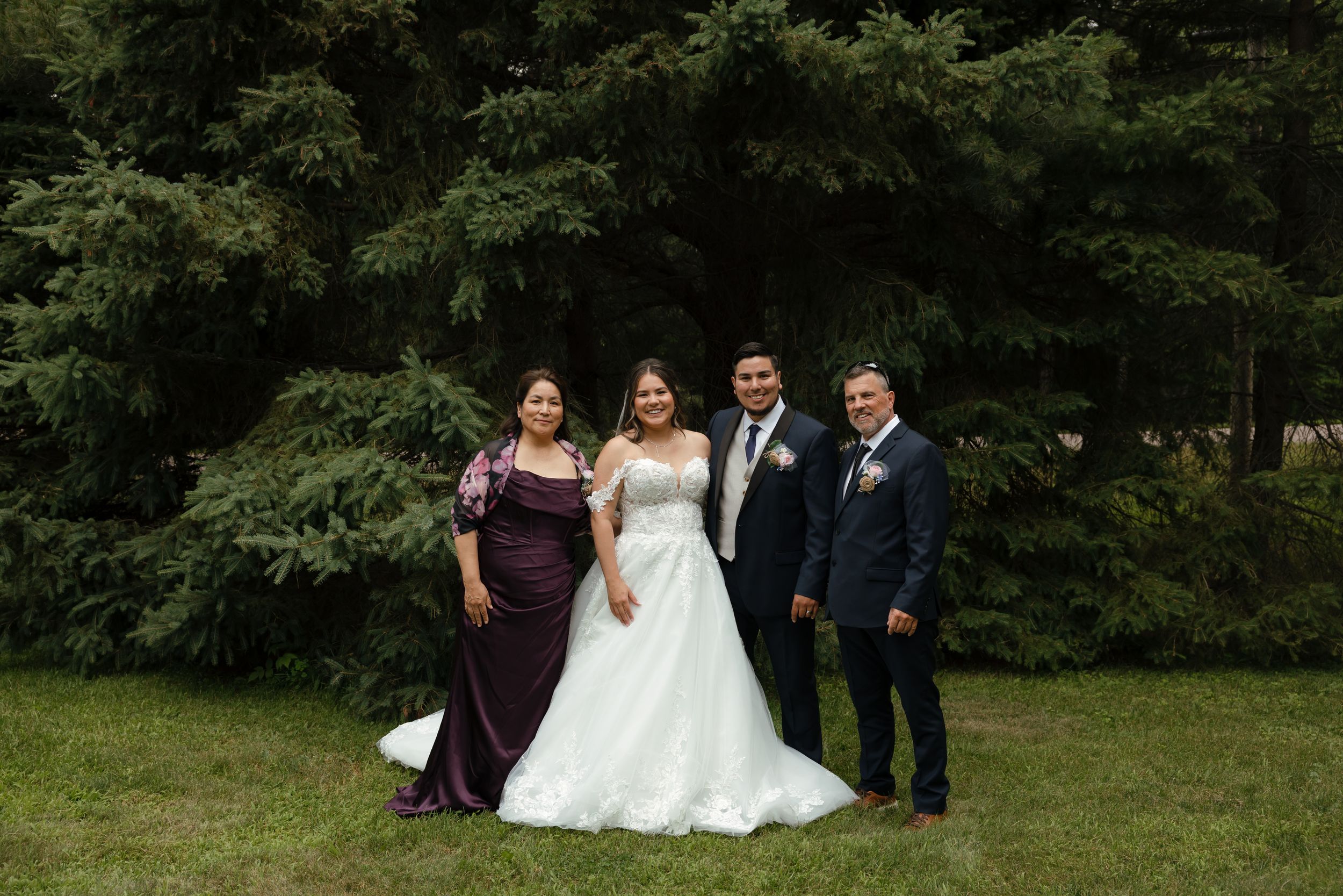 Group of people posing together outdoors in formal attire on grassy landscape with trees in background.