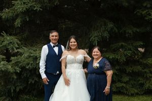 Wedding couple and attendants smile together outdoors in front of green foliage.