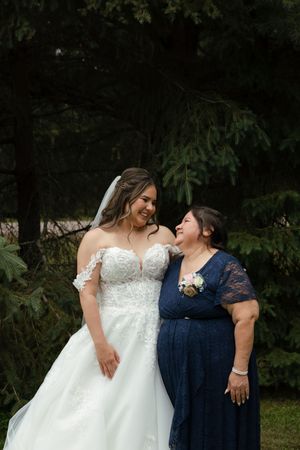 A tender moment between two people at a wedding, with a white bridal gown and navy blue dress against a dark forest backdrop.