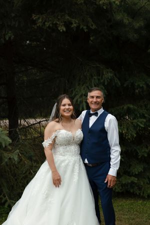 Bride in lace gown and groom in navy blue vest pose for formal portraits in garden setting.