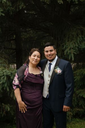 A couple shares a tender moment in their formal attire against a dark foliage backdrop.