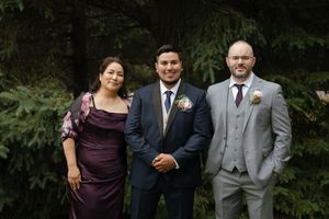 Wedding party wearing purple and grey attire walks through a garden setting during an outdoor celebration.