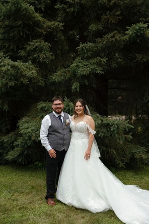 An elegant outdoor wedding portrait showing a couple in formal attire against a backdrop of lush green trees.