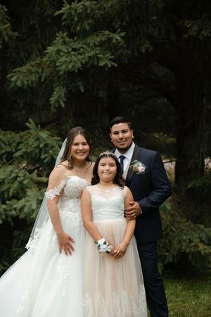 A wedding party in formal attire poses together outdoors with bridesmaids in light dresses.