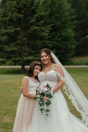 Three bridesmaids in blush dresses stand with a bride in a sparkling white gown holding floral bouquets at an outdoor venue.