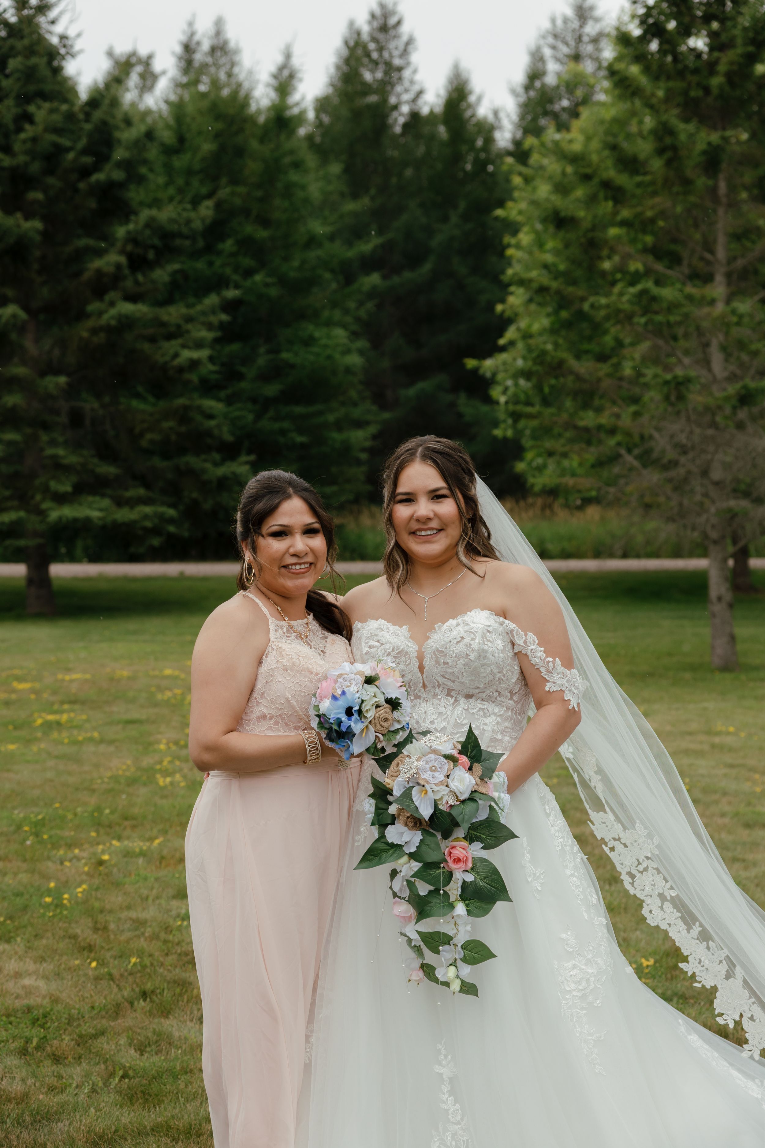 Wedding party poses in a beautiful outdoor garden setting with green trees and grass in the background.