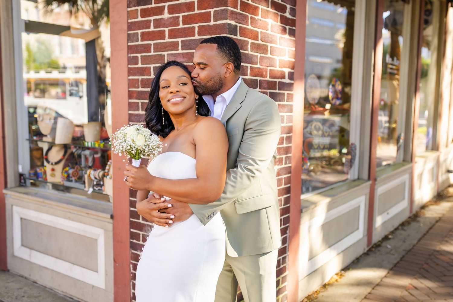 A newlywed couple shares a romantic moment outside a brick storefront.