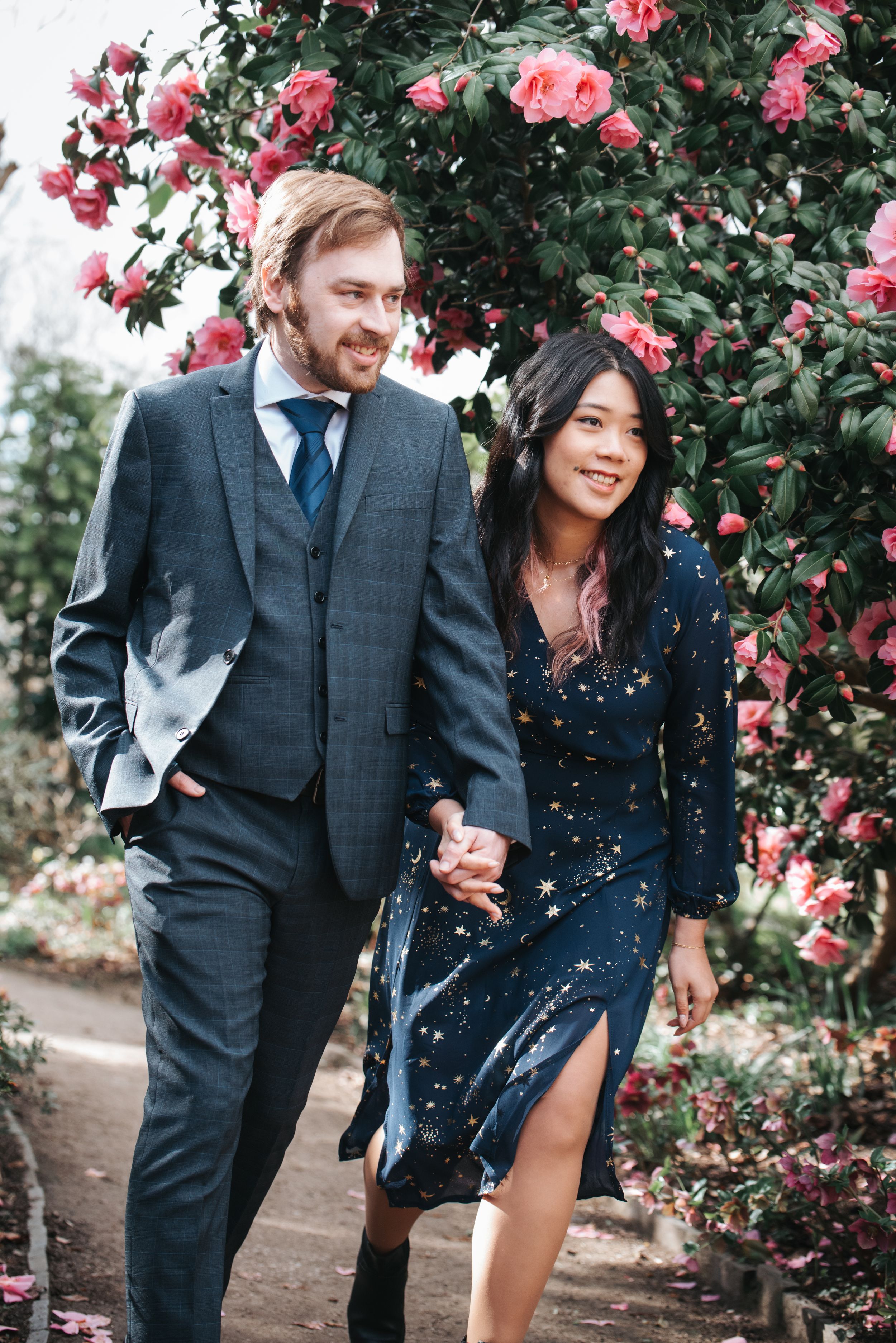 Couple laughing together in front of pink rose bushes in formal attire.