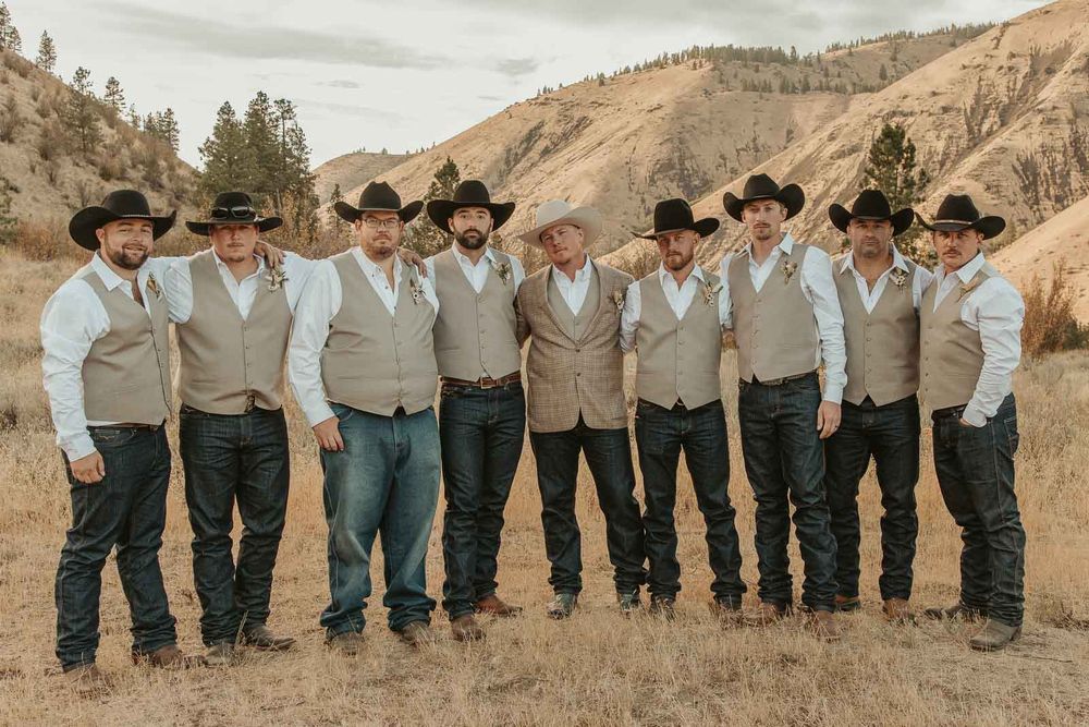Groomsmen in cowboy hats and taupe vests, sharing laughs with groom. American Homestead venue.  by Spokane wedding photographer