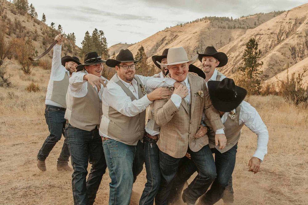 Groomsmen in cowboy hats and taupe vests, sharing laughs with groom. American Homestead venue.  by Spokane wedding photographer