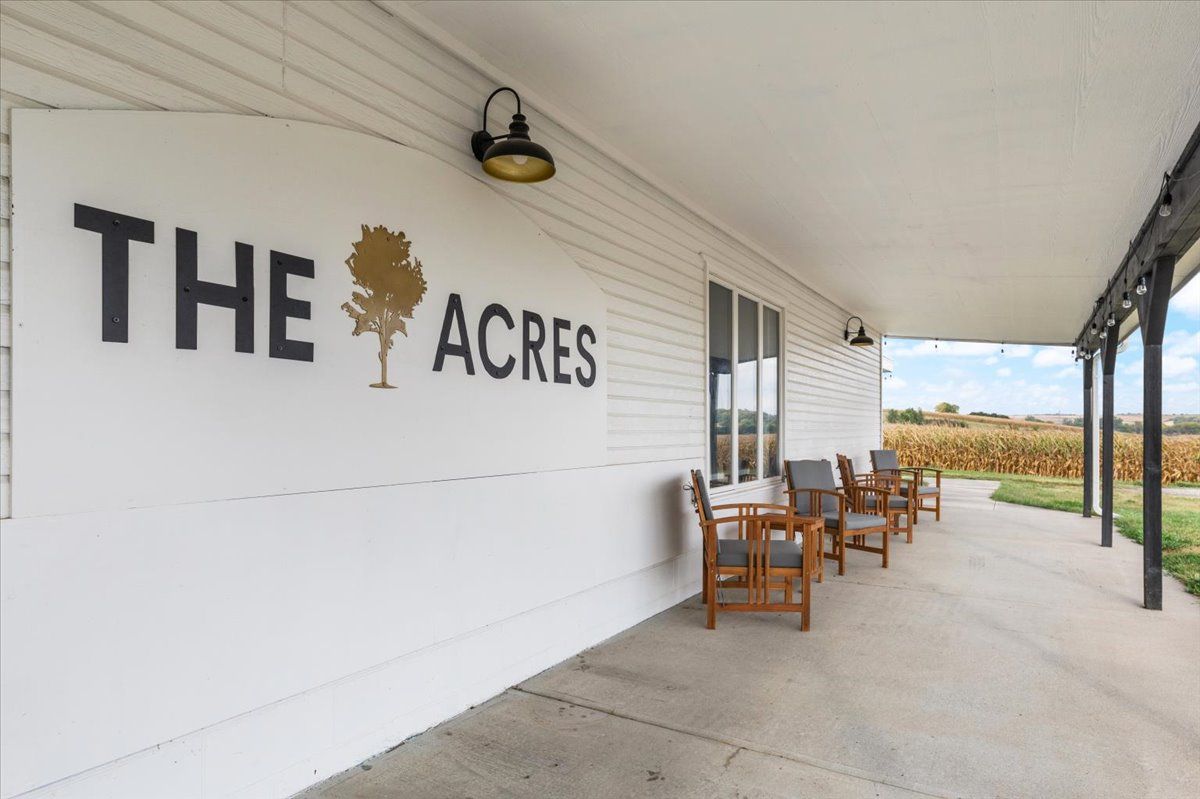 Exterior porch of The Acres venue with wooden chairs overlooking a scenic countryside landscape.