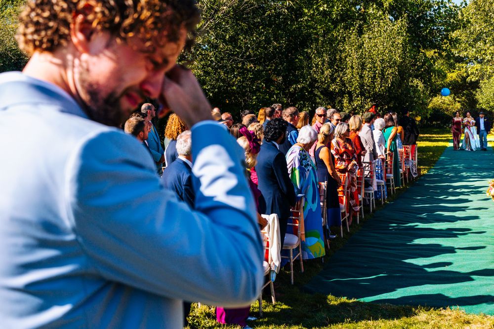 Emotional groom crying during outdoor wedding ceremony with guests seated in rows on a sunny day.