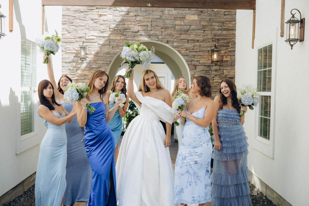 A group in formal attire celebrating under a white archway with brick and stone walls at a wedding celebration.