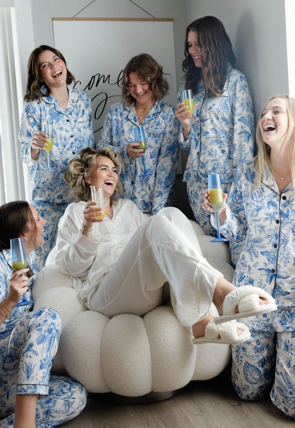 A group in matching blue and white floral pajamas enjoying drinks and laughter together on a plush chair.