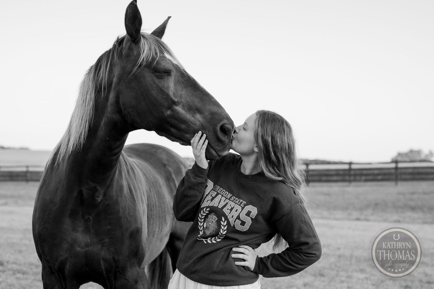 Black and white photo of someone bonding with their horse in a fenced pasture.