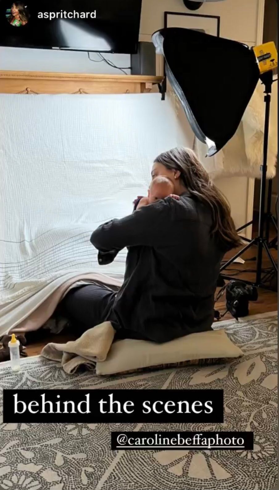 Behind the scenes of a newborn photography session with a photographer sitting on the floor holding a baby.