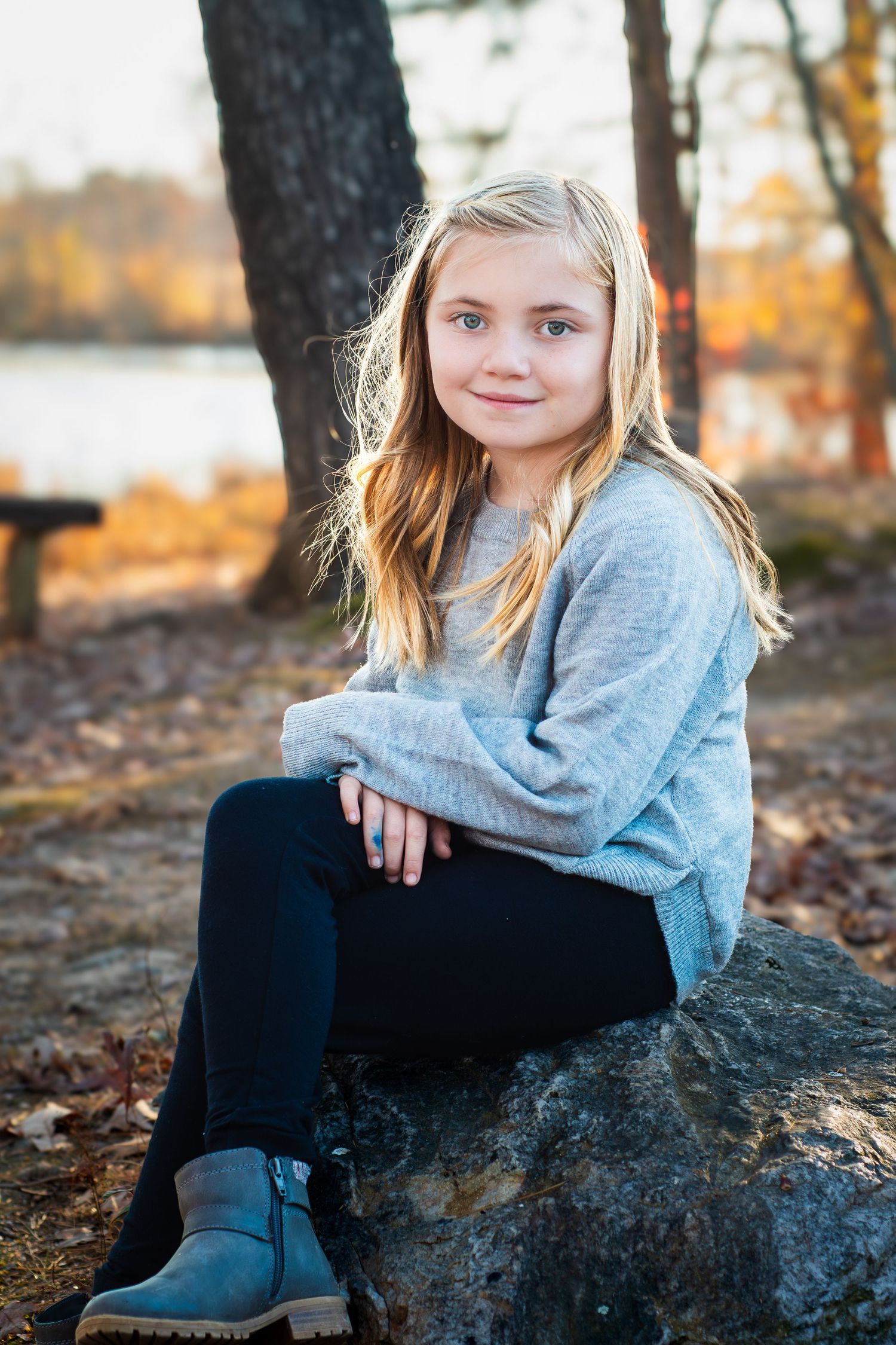 Young person in gray sweater sitting on rock during autumn near lake.