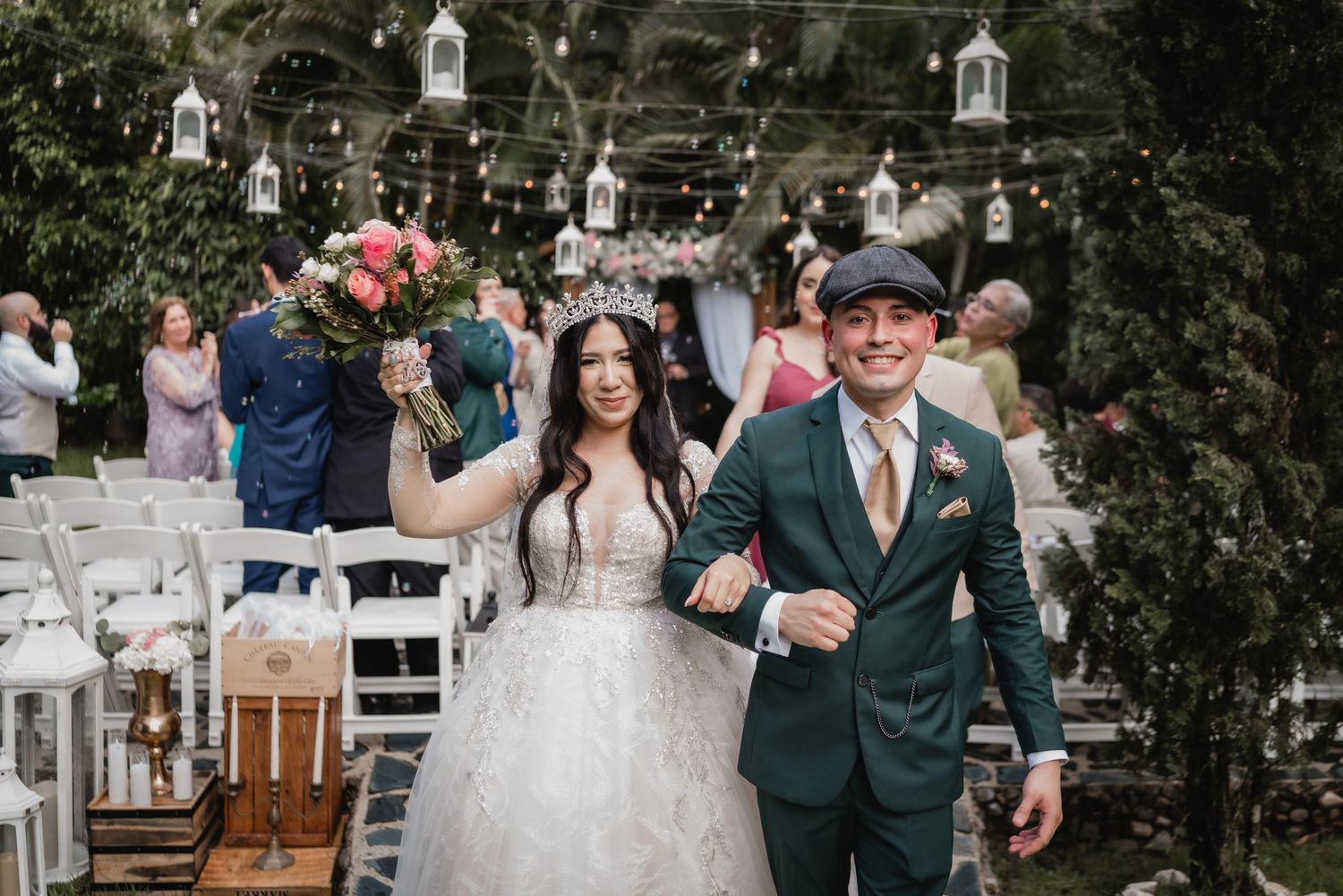 A couple celebrates at their outdoor garden wedding with white chairs and hanging lanterns decorating the venue.