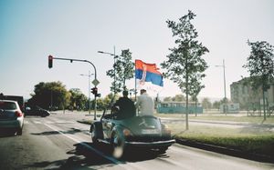 Fotografisanje venčanja na ulicama grada Novog Sada u mladenačkom autu bez krova voze se mladoženja i kum. 
Zastava Srbije