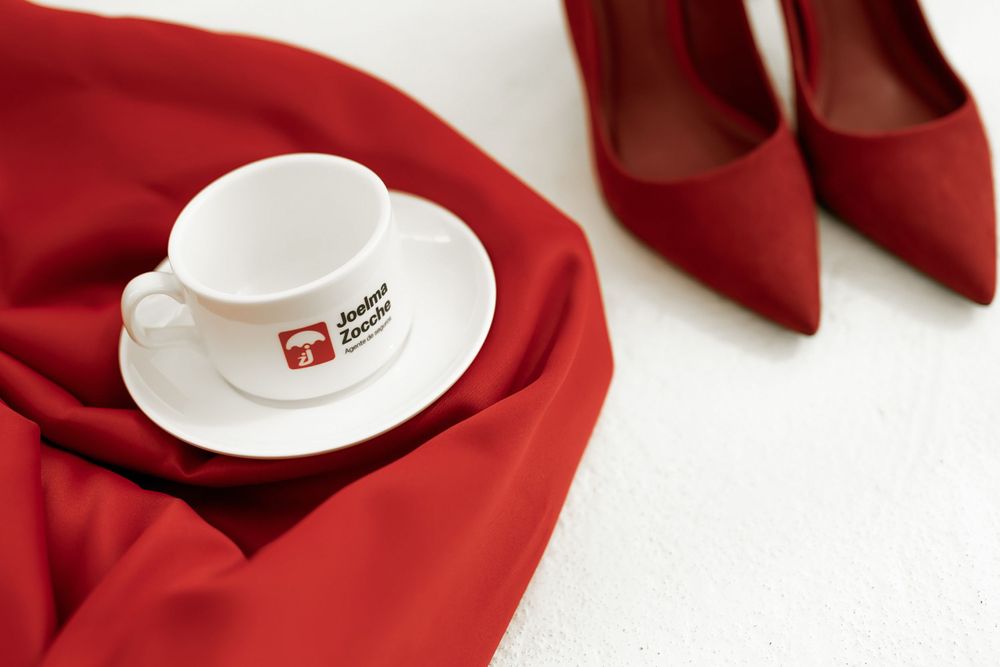 White coffee cup on red fabric next to elegant red stiletto heels in a minimalist fashion composition.