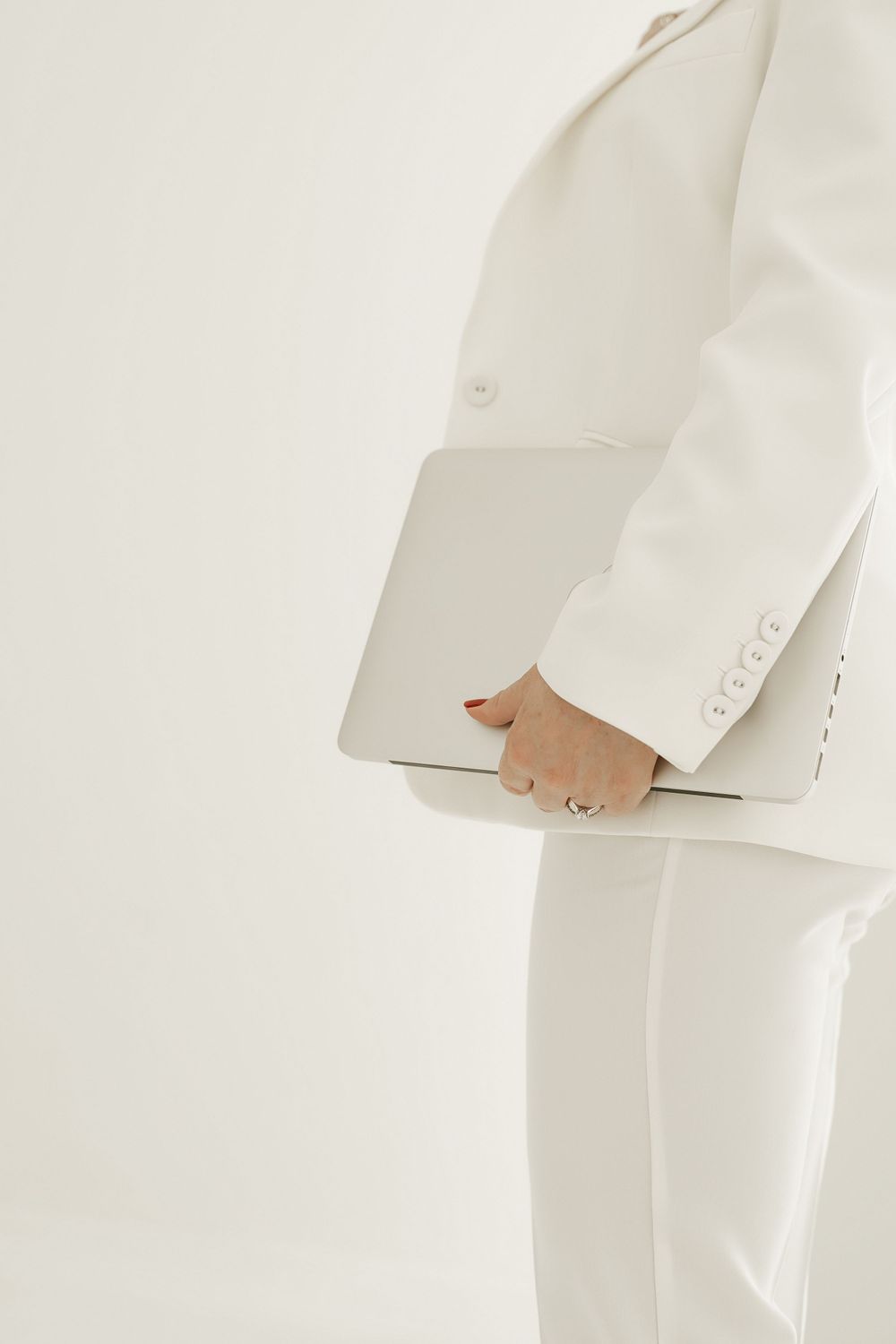 Close-up detail of a white formal suit sleeve and hand against a minimalist light background.