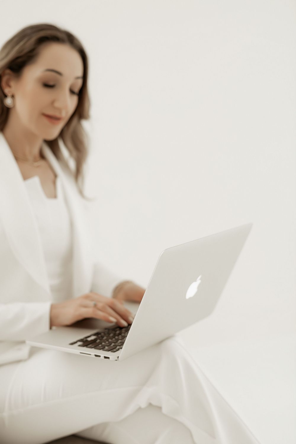 Person in white attire working on MacBook laptop while sitting against light background.