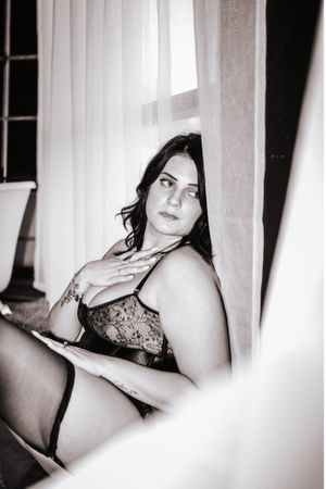 Black and white boudoir photo near window with lace lingerie.