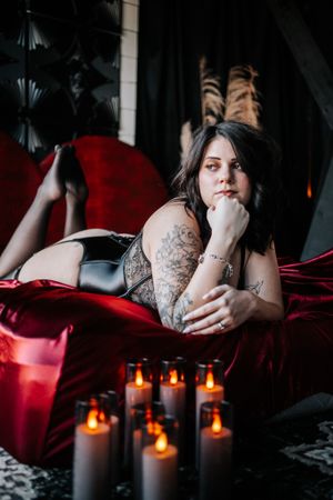 Moody boudoir photo on red velvet with candles in dark setting.