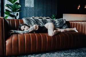 Moody boudoir scene on brown leather couch with dark teal walls and hanging lights.