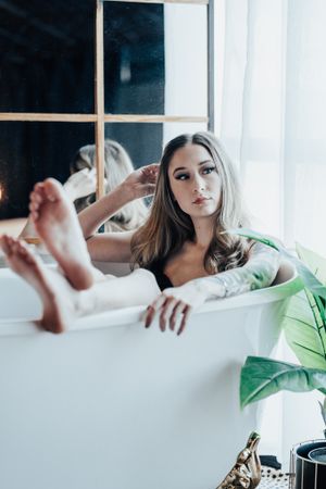 Artistic bathtub scene with green tropical leaves and natural window light.