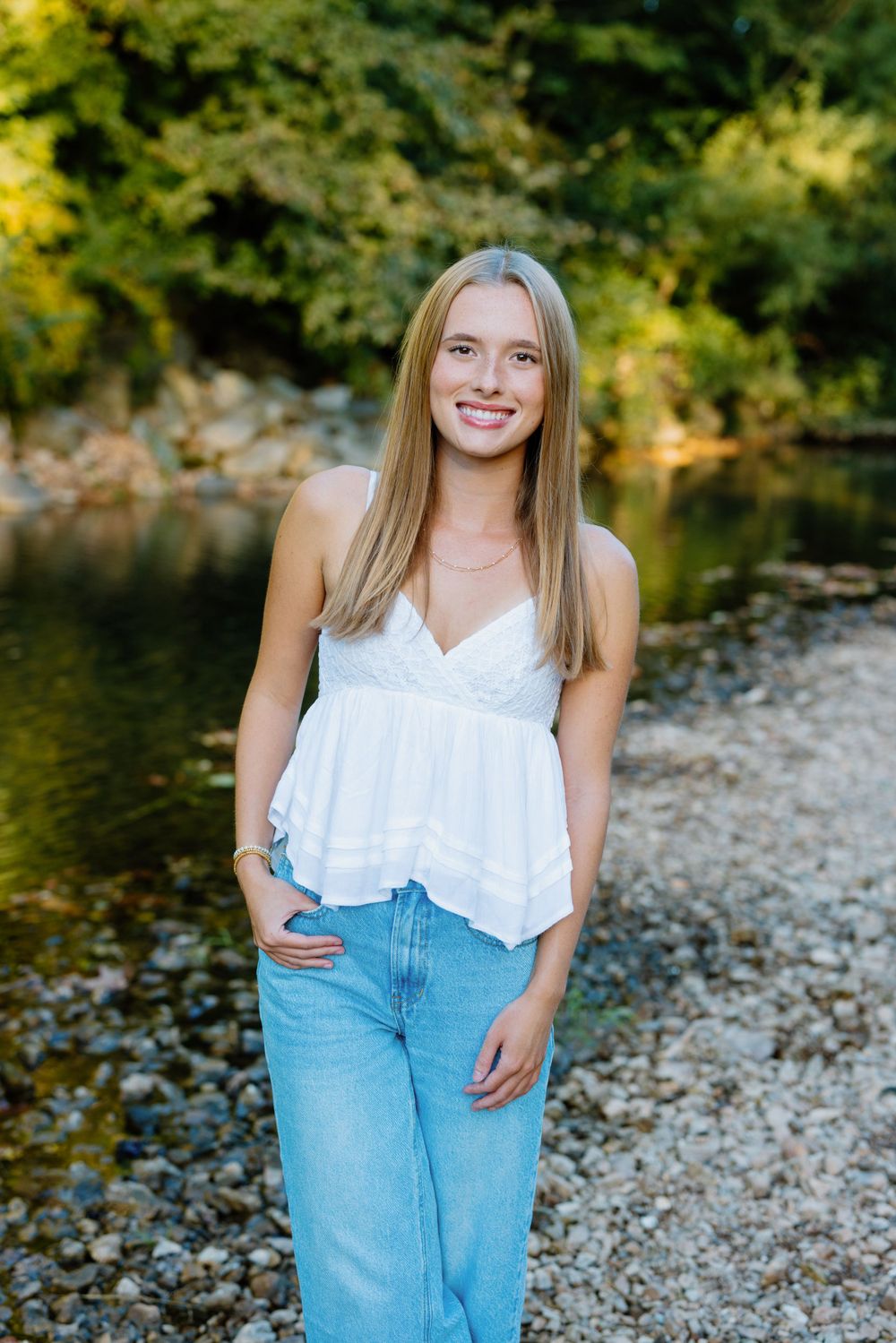 Casual outdoor portrait by river with rocky shore and forest scenery.