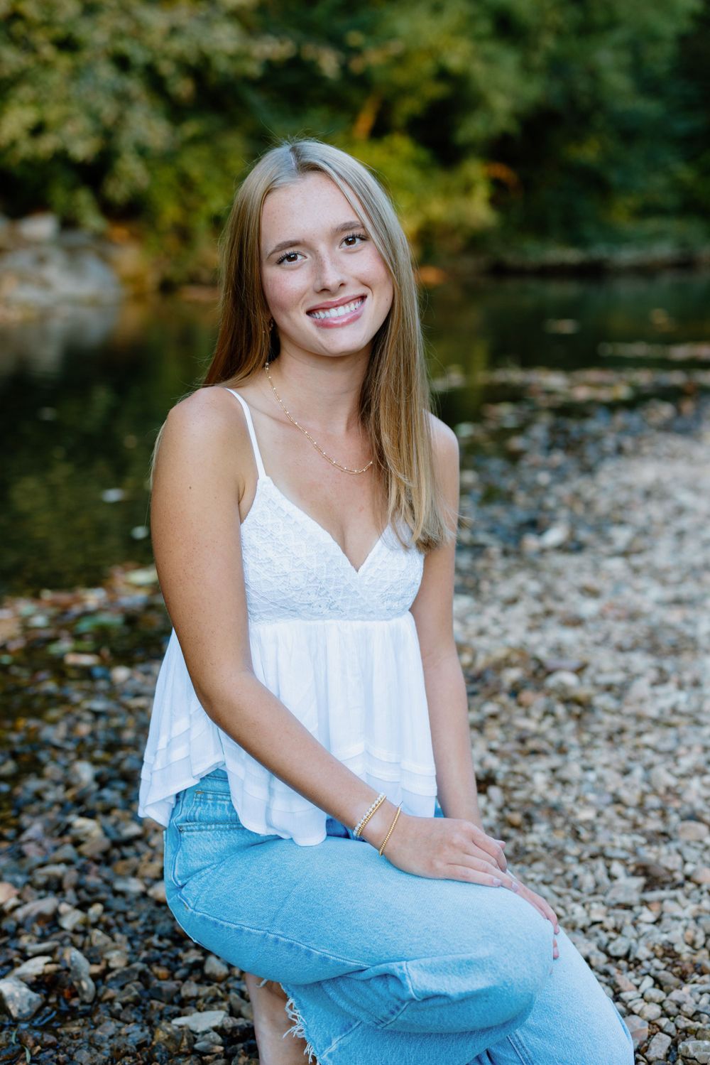 Natural outdoor portrait by water with autumn foliage in background.