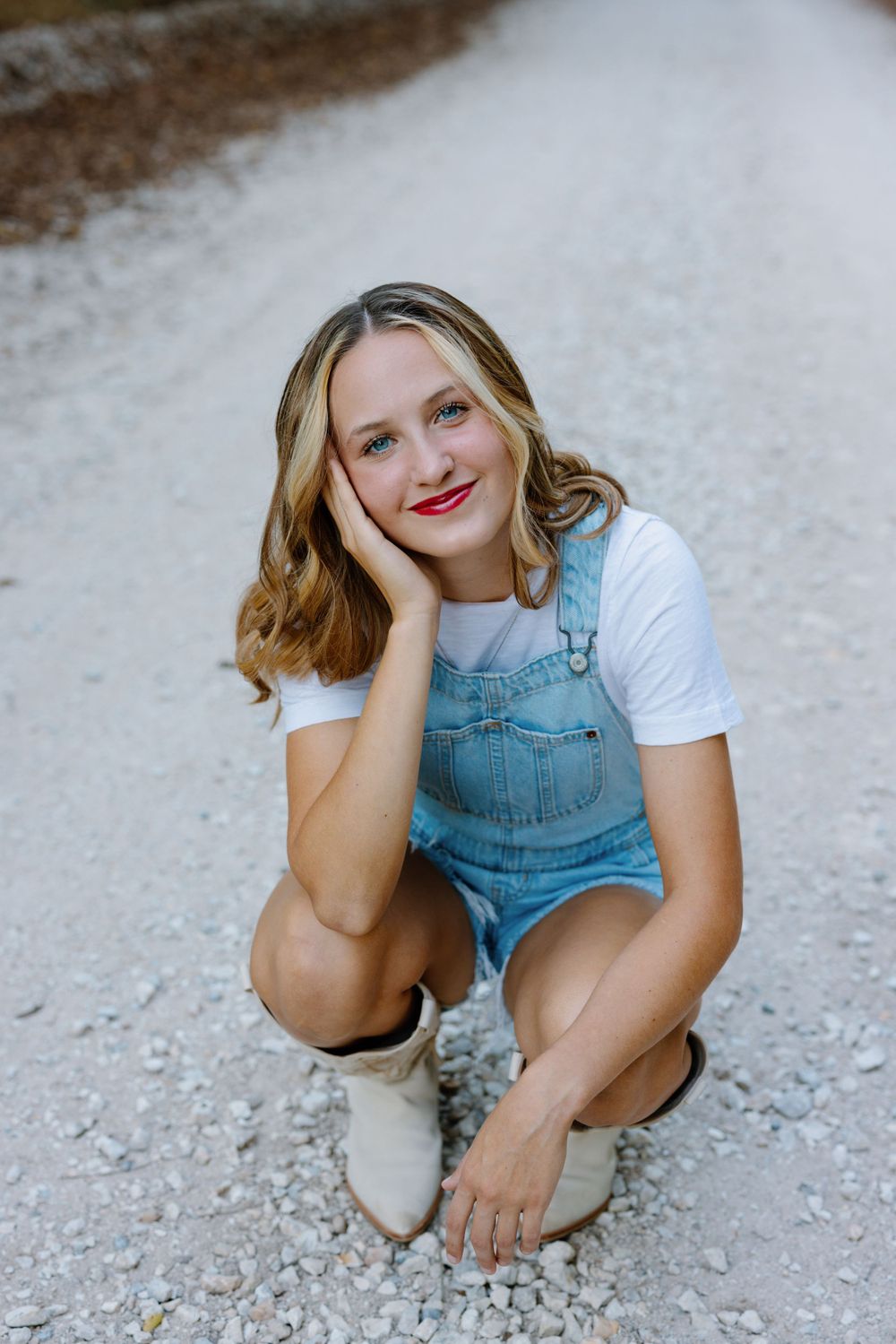 Casual portrait in denim overalls and white boots on gravel path.