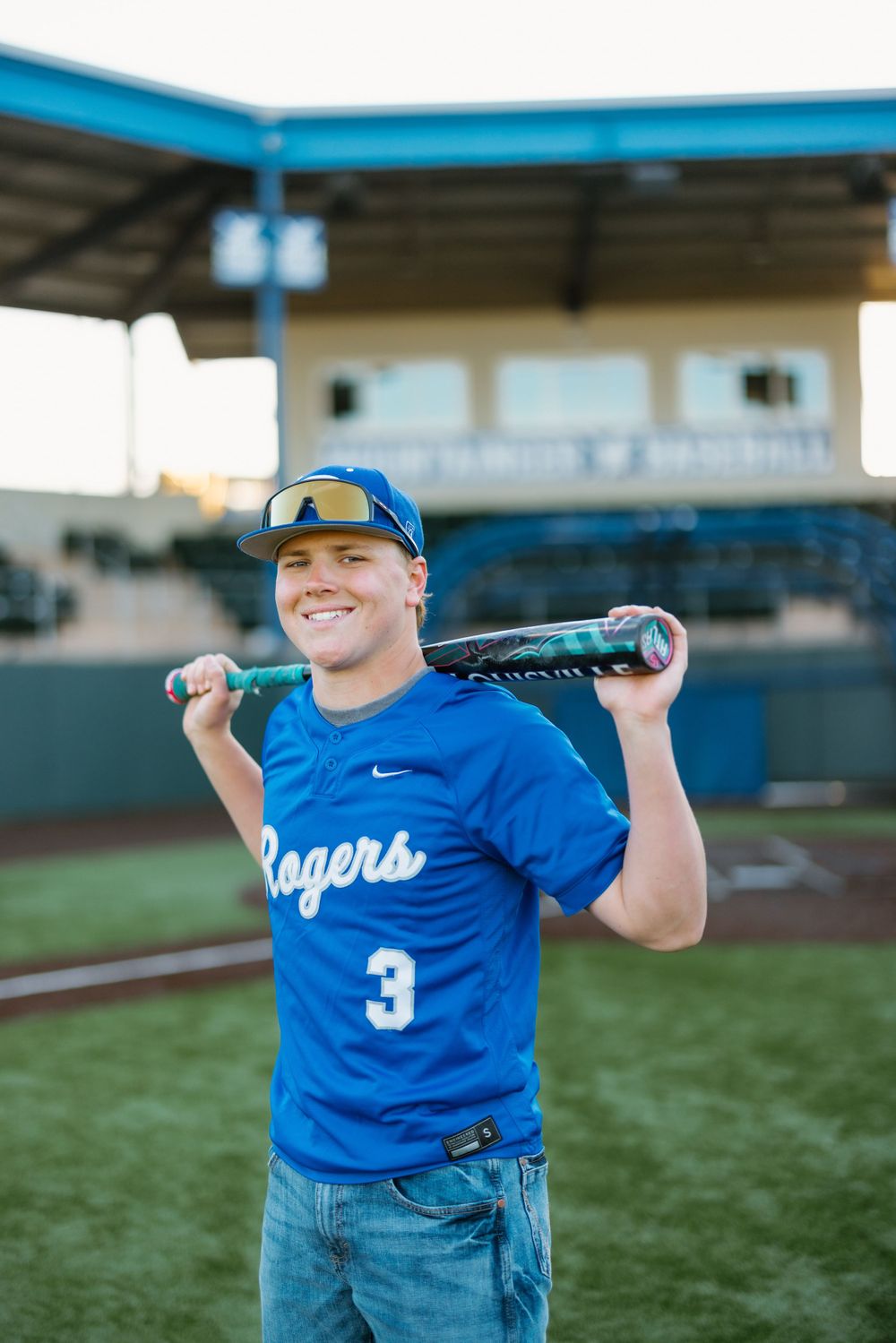 A baseball player in a blue Rogers jersey number 3 poses with a bat on their shoulder at a baseball field.