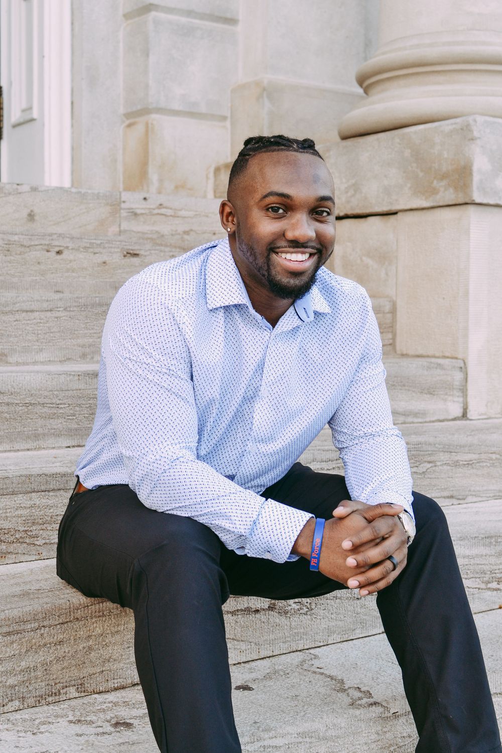 Professional in light blue dress shirt sitting on stone steps of building.