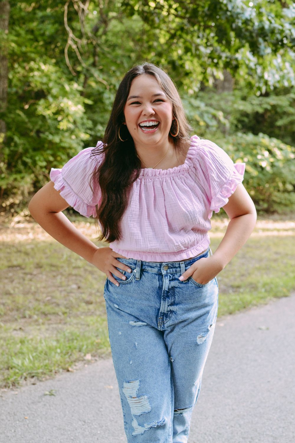 Candid outdoor portrait of a woman in pink ruffle top and distressed jeans.