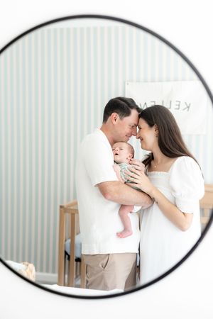 Happy parents smile at each other while holding their newborn baby in a softly decorated nursery room.