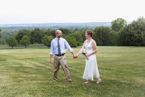 Bride and groom holding hands walking across green lawn with scenic countryside backdrop on their wedding day.