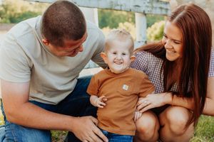 Happy young family with smiling toddler boy sitting outdoors in a casual photo session.