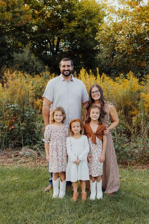 Family of five posing outdoors in coordinated fall outfits, with autumn foliage in the background.