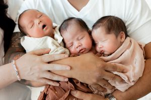 Three sleeping newborn triplets cradled in parents hands, wrapped in soft blankets, peaceful newborn photography.