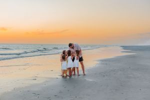 Family of four enjoying a beautiful sunset on the beach, with golden orange skies reflecting on the calm ocean waves.
