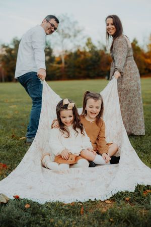 Family sitting together on white lace blanket in grassy field during autumn sunset.