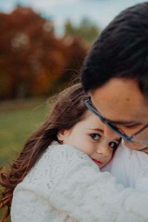 A person wearing glasses and a white sweater gazes softly in an autumn outdoor setting with blurred bokeh background.