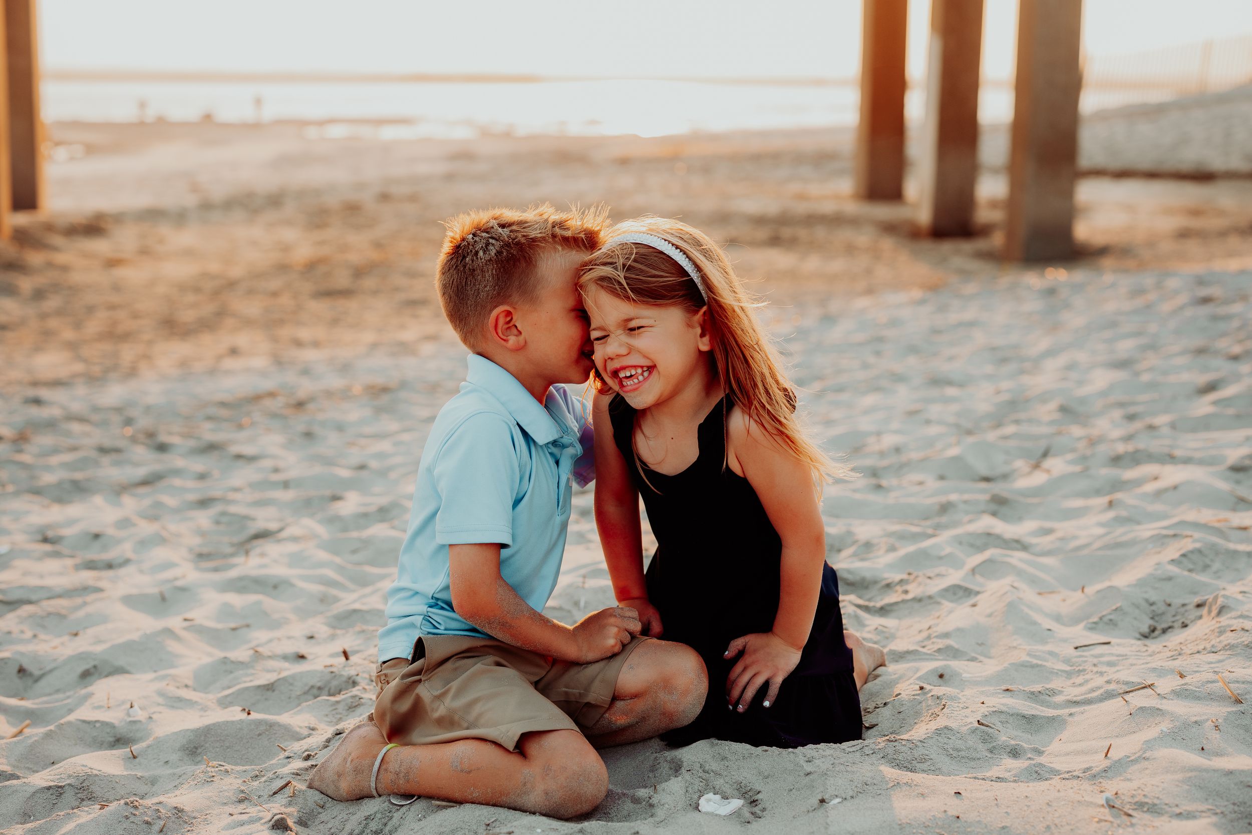 A romantic sunset moment shared on a sandy beach under wooden pier posts.