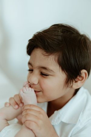 A young child in a white shirt smiles playfully while holding their hands near their face.