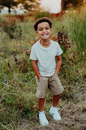 A young child in a light blue t-shirt and khaki shorts plays joyfully in a grassy field on a sunny day.