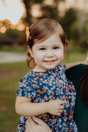 A smiling toddler wearing a navy blue floral dress plays outdoors in warm sunset lighting.